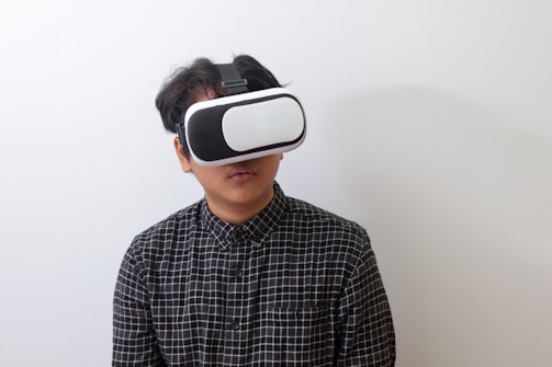 A person wearing a black and white plaid shirt uses a virtual reality headset against a plain white background.