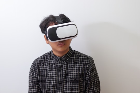 A person wearing a black and white plaid shirt uses a virtual reality headset against a plain white background.