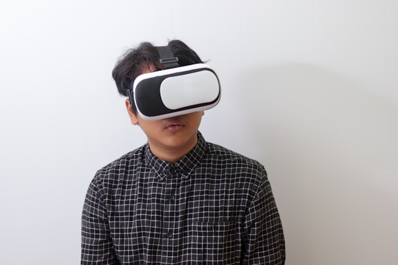 A person wearing a black and white plaid shirt uses a virtual reality headset against a plain white background.
