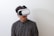 A person wearing a black and white plaid shirt uses a virtual reality headset against a plain white background.