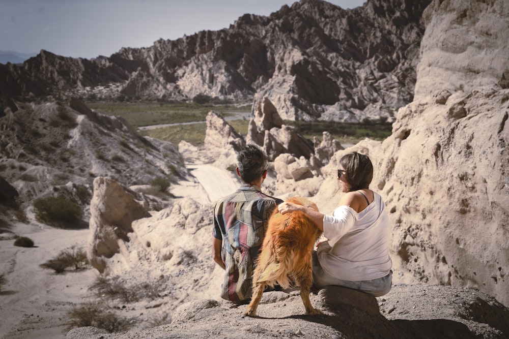 a man and a woman sitting on a rock with a dog