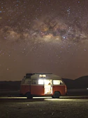 Night sky filled with stars above a cozy van setup illuminated from inside.