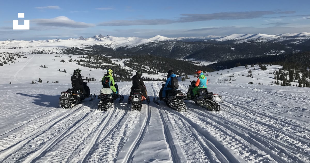 A group of people riding snowmobiles down a snow covered slope photo ...