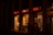 A storefront at night with bright orange signs displaying 'SPACE 23'. The windows are illuminated, showcasing a mannequin dressed in white and various merchandise. Several people are standing outside, partially visible in the dim light.