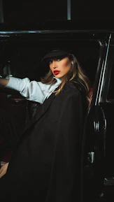 A stylish woman wearing jm bella lipstick and a chic hat, smiling confidently.