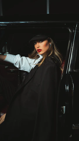 A stylish woman wearing jm bella lipstick and a chic hat, smiling confidently.