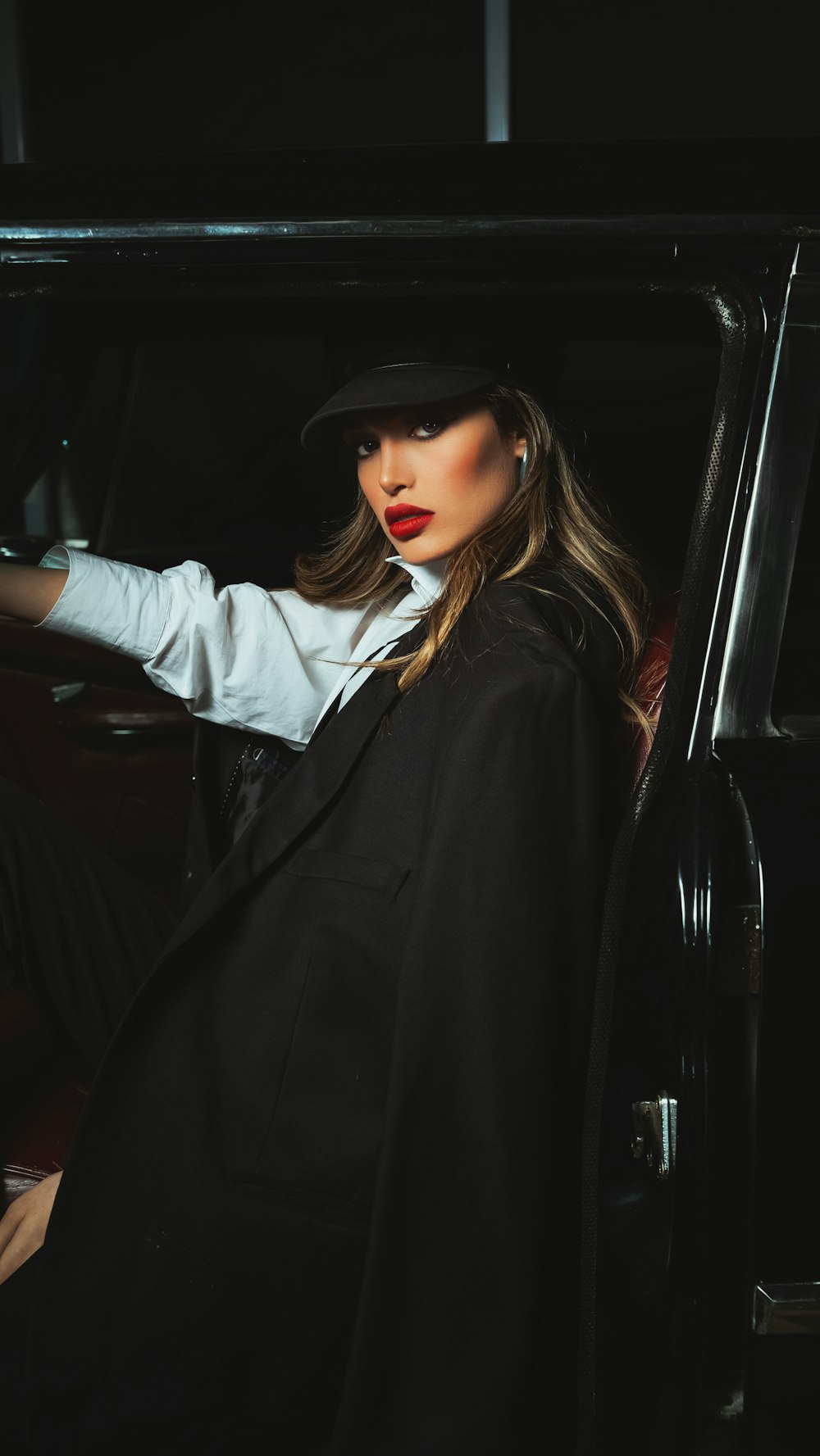 a woman sitting in a car wearing a hat and coat