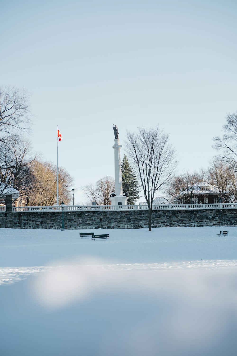 a snowy park with benches and a monument in the background