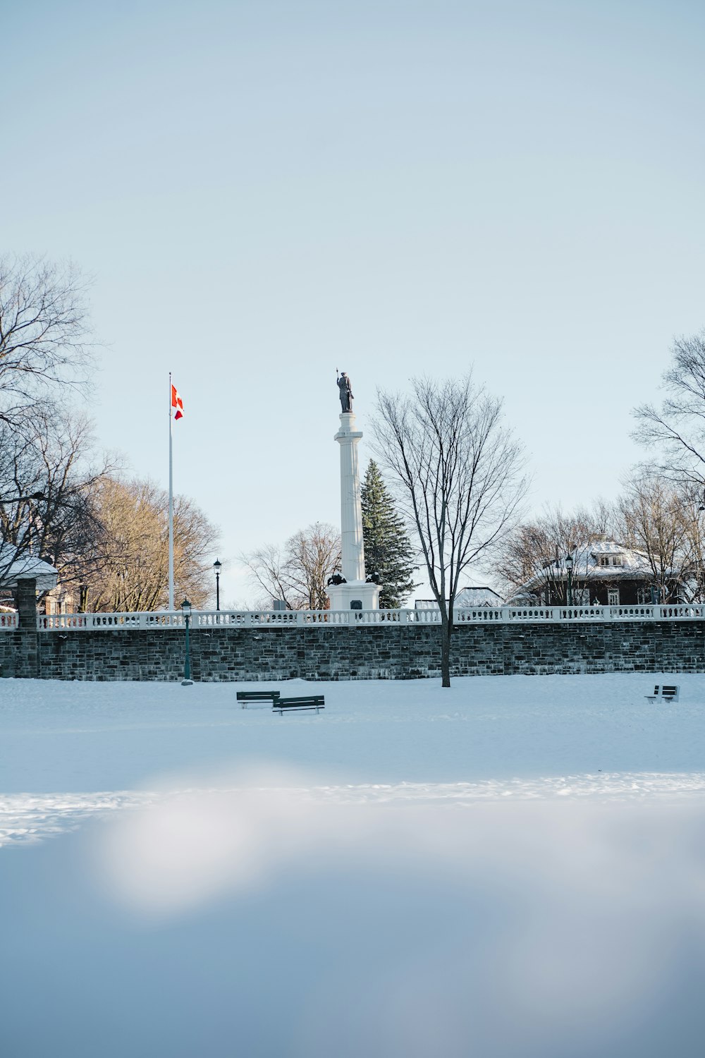 ein verschneiter Park mit Bänken und einem Denkmal im Hintergrund