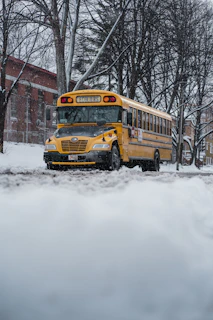 An early morning view of a school bus parked outside a modern school building with students waiting.