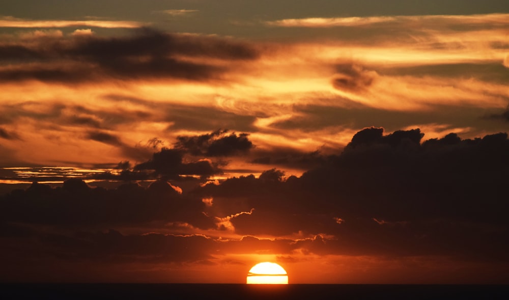 the sun is setting over the ocean with clouds