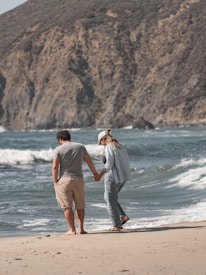 a man and a woman walking on the beach holding hands