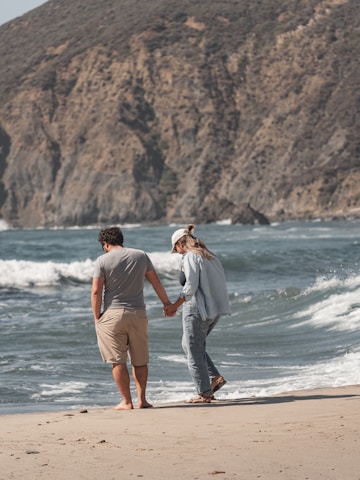 a man and a woman walking on the beach holding hands