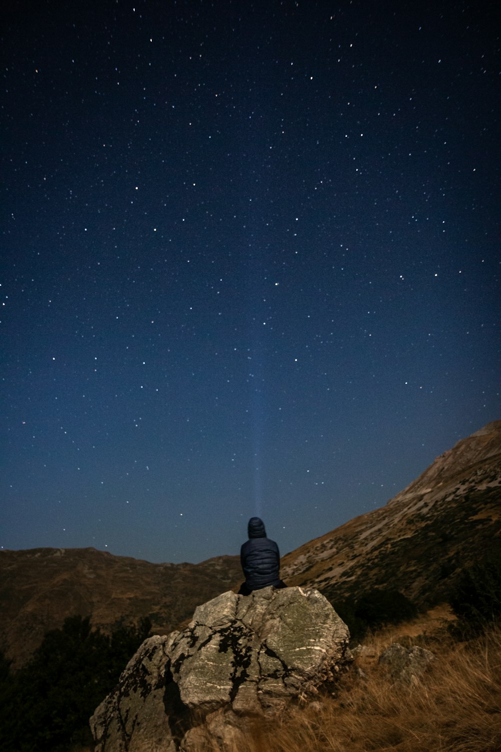 a person sitting on top of a rock under a night sky
