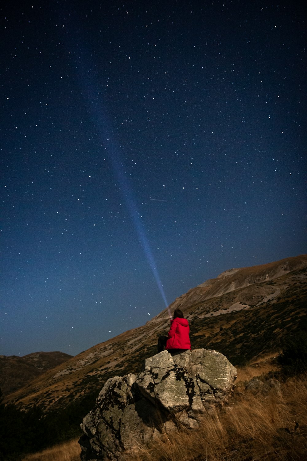 a person sitting on top of a rock under a night sky