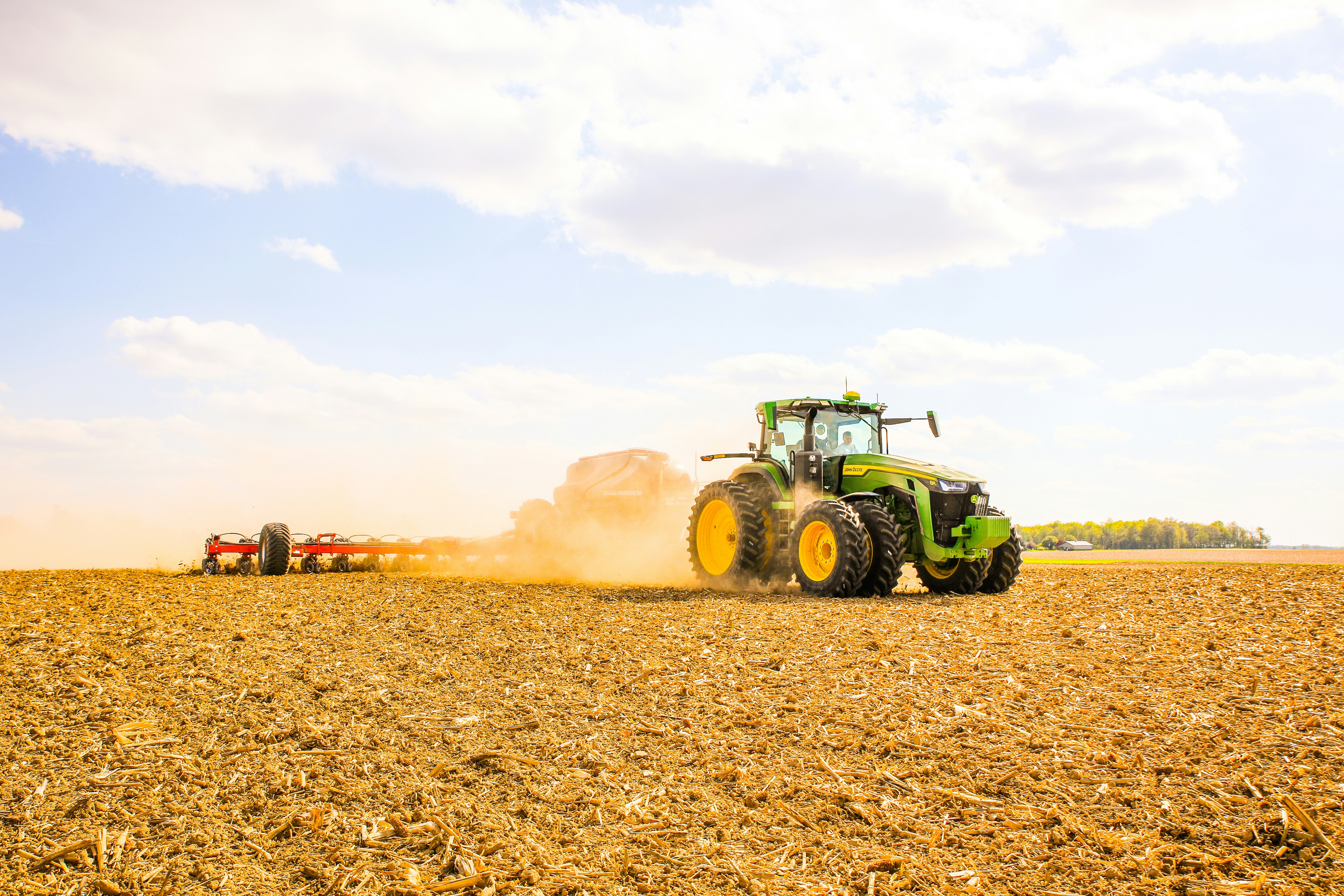 A tractor ploughing a vast, green field under a blue sky