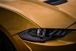 Close-up of a yellow sports car’s headlight and grille under bright daylight.