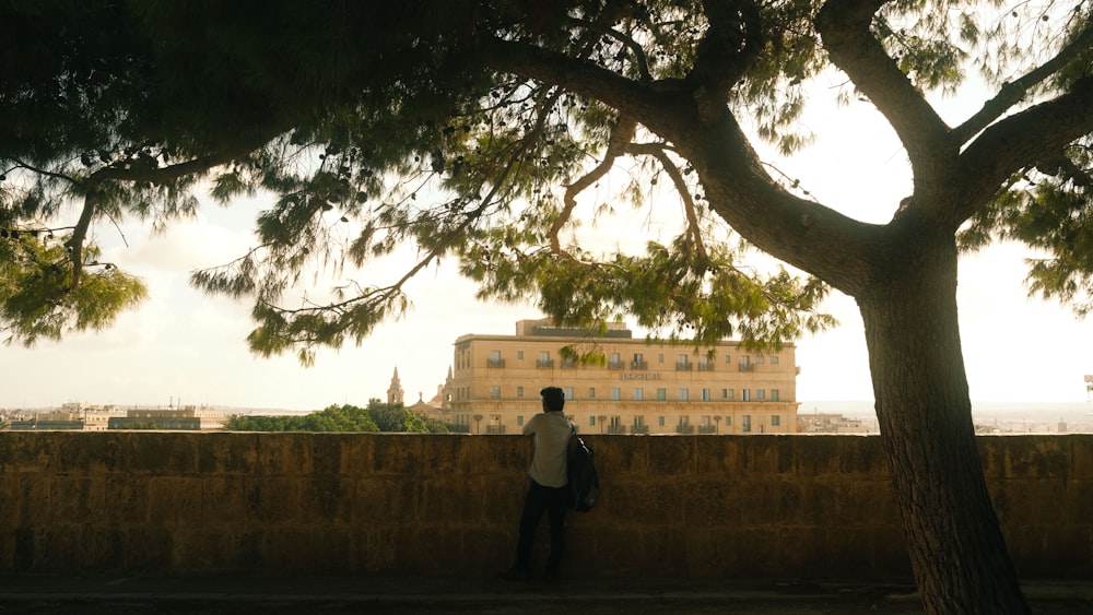 a man standing next to a tree near a wall