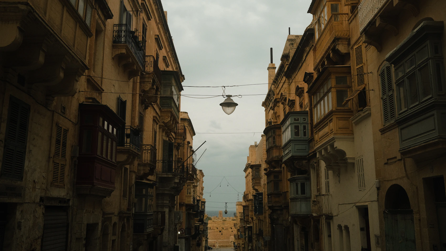 A shadowed Valletta street with enclosed timber balconies leading towards the sea