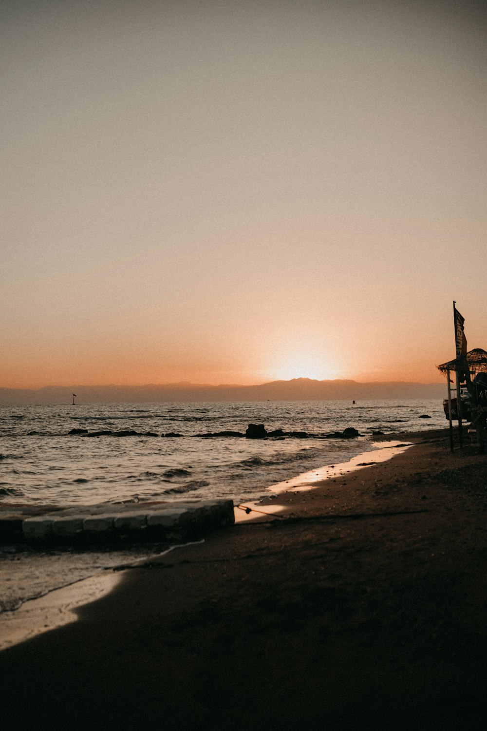 the sun is setting over the ocean with a beach chair in the foreground