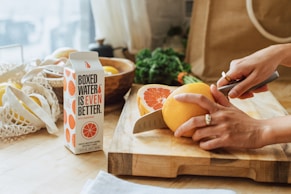 a person cutting an orange on a cutting board