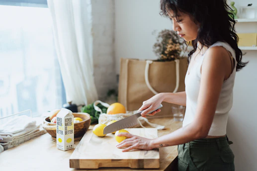 A vibrant woman in her 40s enjoying a refreshing lemon water in a sunlit modern kitchen.