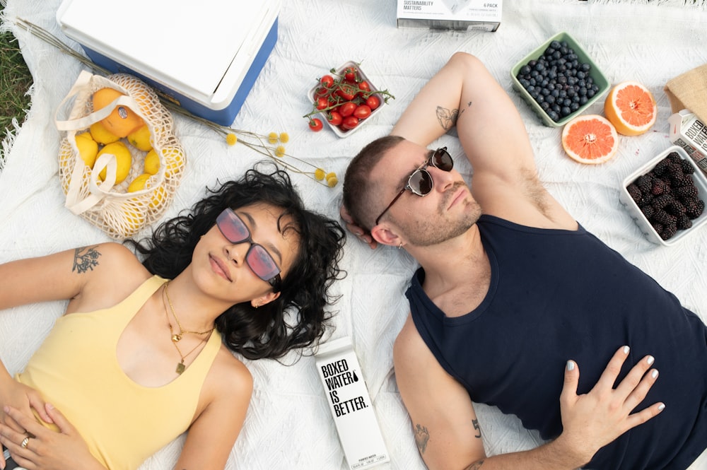 a man and a woman laying on a blanket with fruit