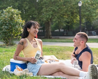 a man and a woman sitting on a blanket in a park