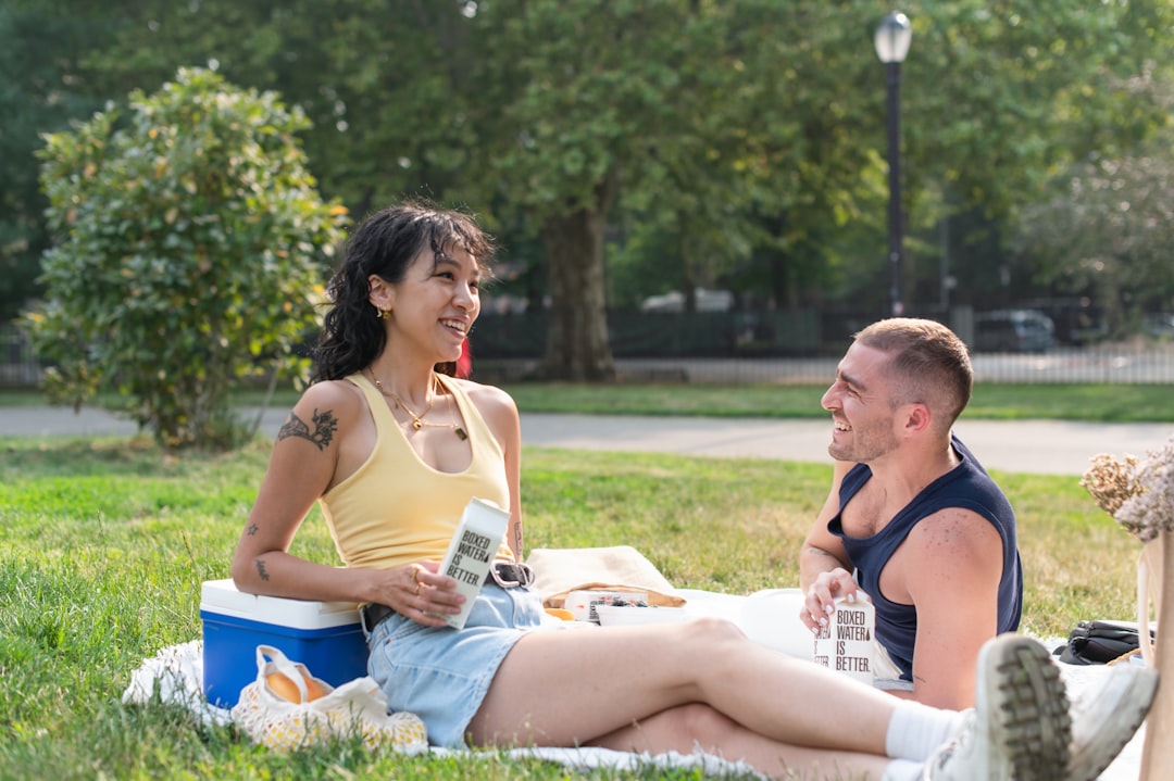 a man and a woman sitting on a blanket in a park,