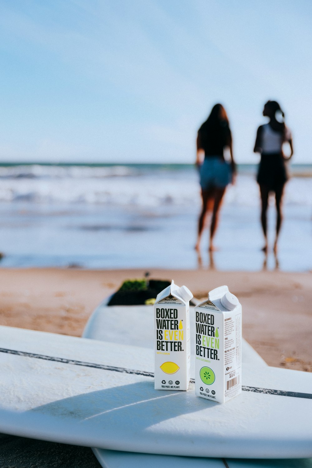 um casal de pessoas caminhando em uma praia ao lado de uma prancha de surf