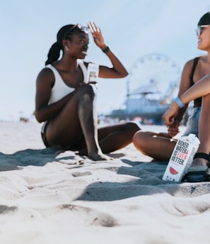 two women sitting in the sand at the beach