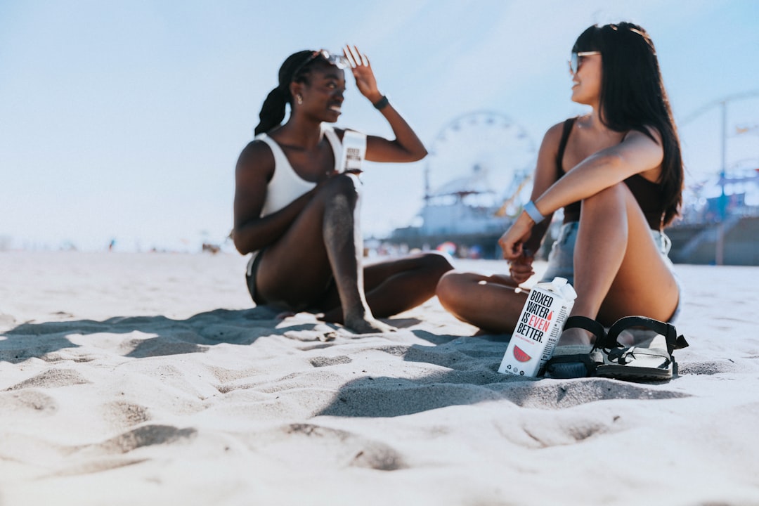 two women sitting in the sand at the beach,