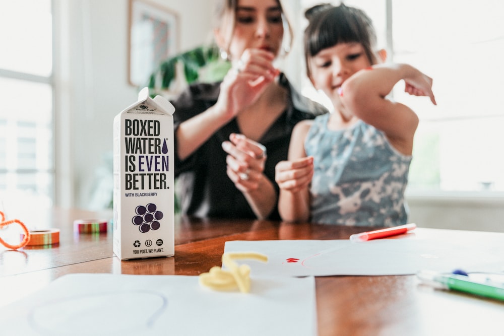 two women sitting at a table with a box of water