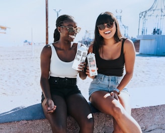 two women sitting next to each other holding a bottle