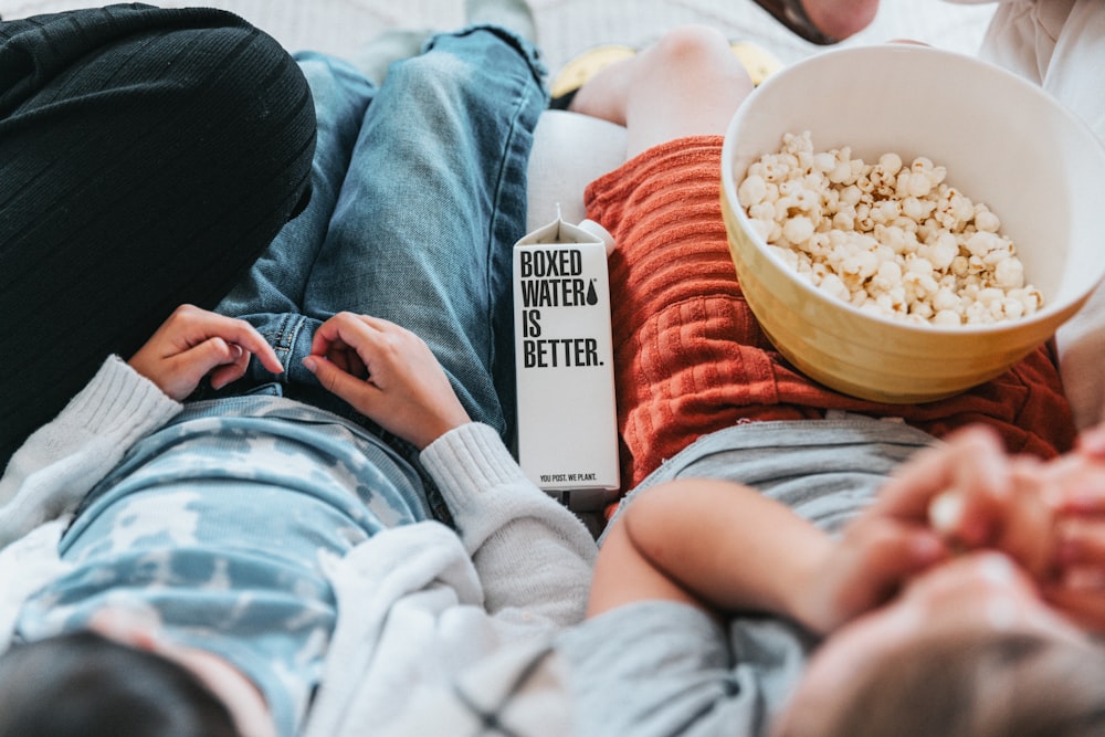 a person laying on a bed next to a bowl of popcorn