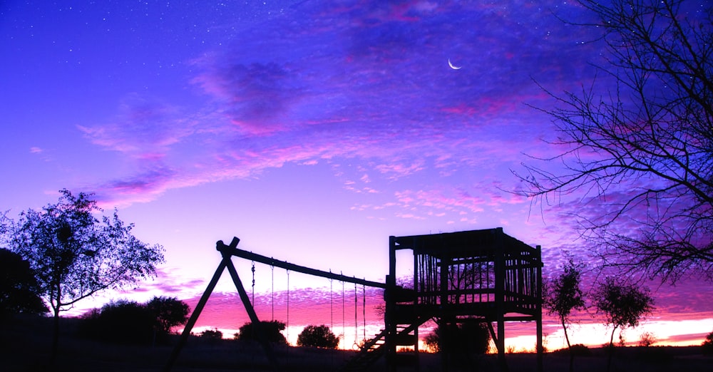 a purple sky with a swing set in the foreground