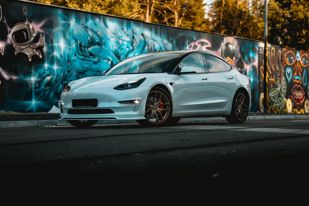 a white car parked in front of a graffiti covered wall