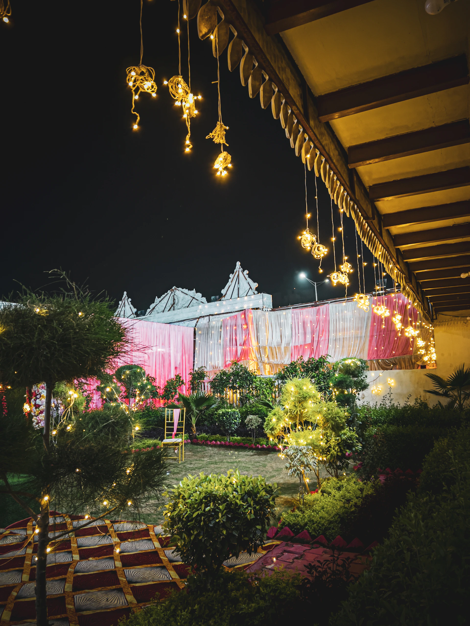An outdoor garden party scene showcasing colorful drapes, chic lounge furniture, and tasteful lighting under the evening sky.