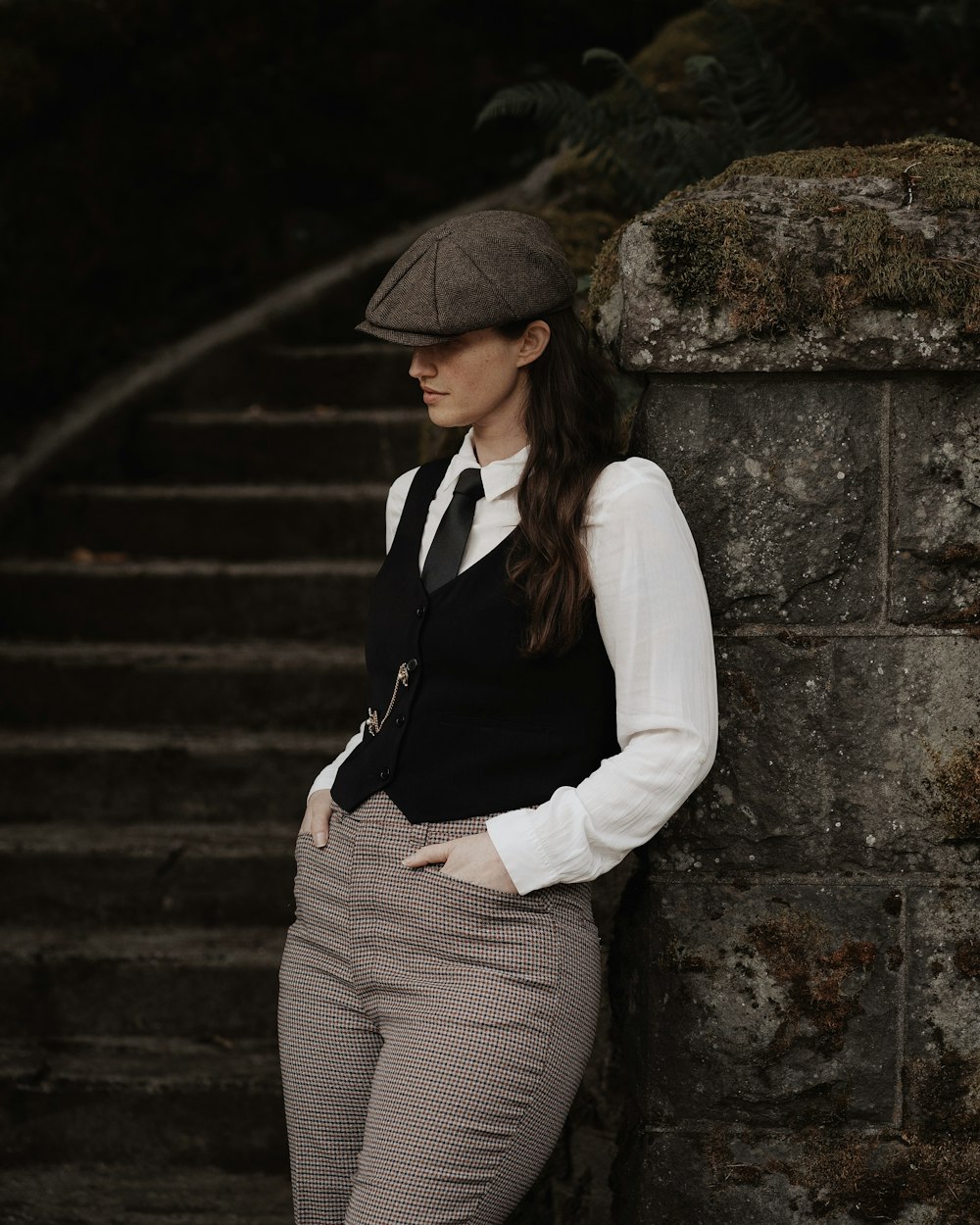 a woman leaning against a stone wall wearing a hat