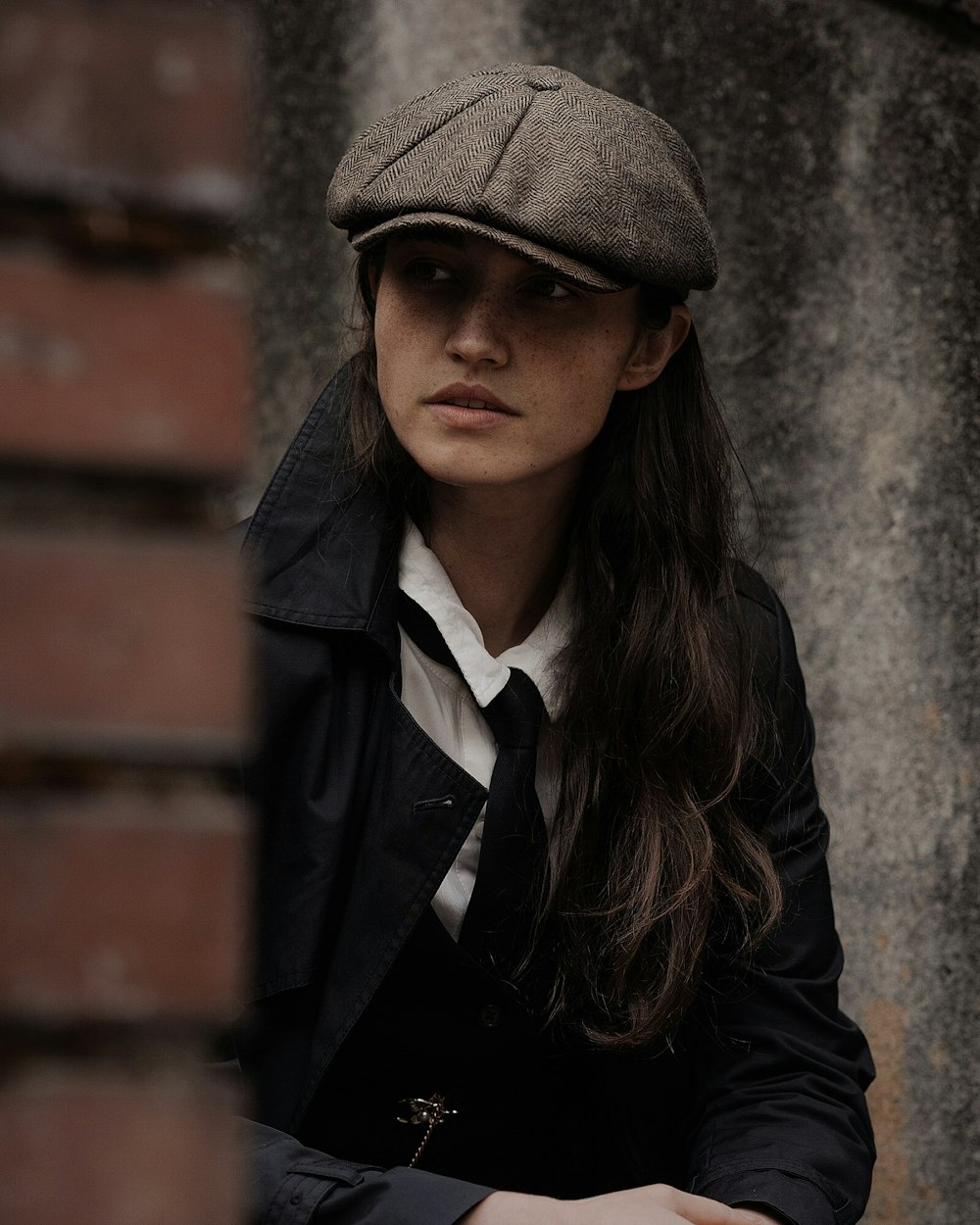 uma mulher usando um chapéu e uma jaqueta encostada em uma parede
