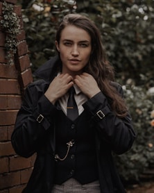 a woman wearing a suit and tie standing next to a brick wall
