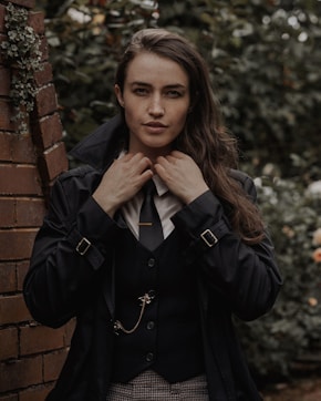 a woman wearing a suit and tie standing next to a brick wall