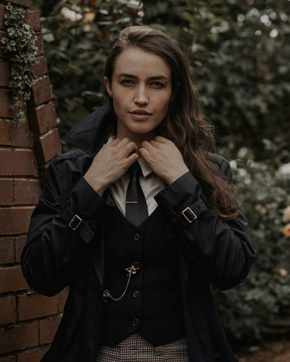 a woman wearing a suit and tie standing next to a brick wall