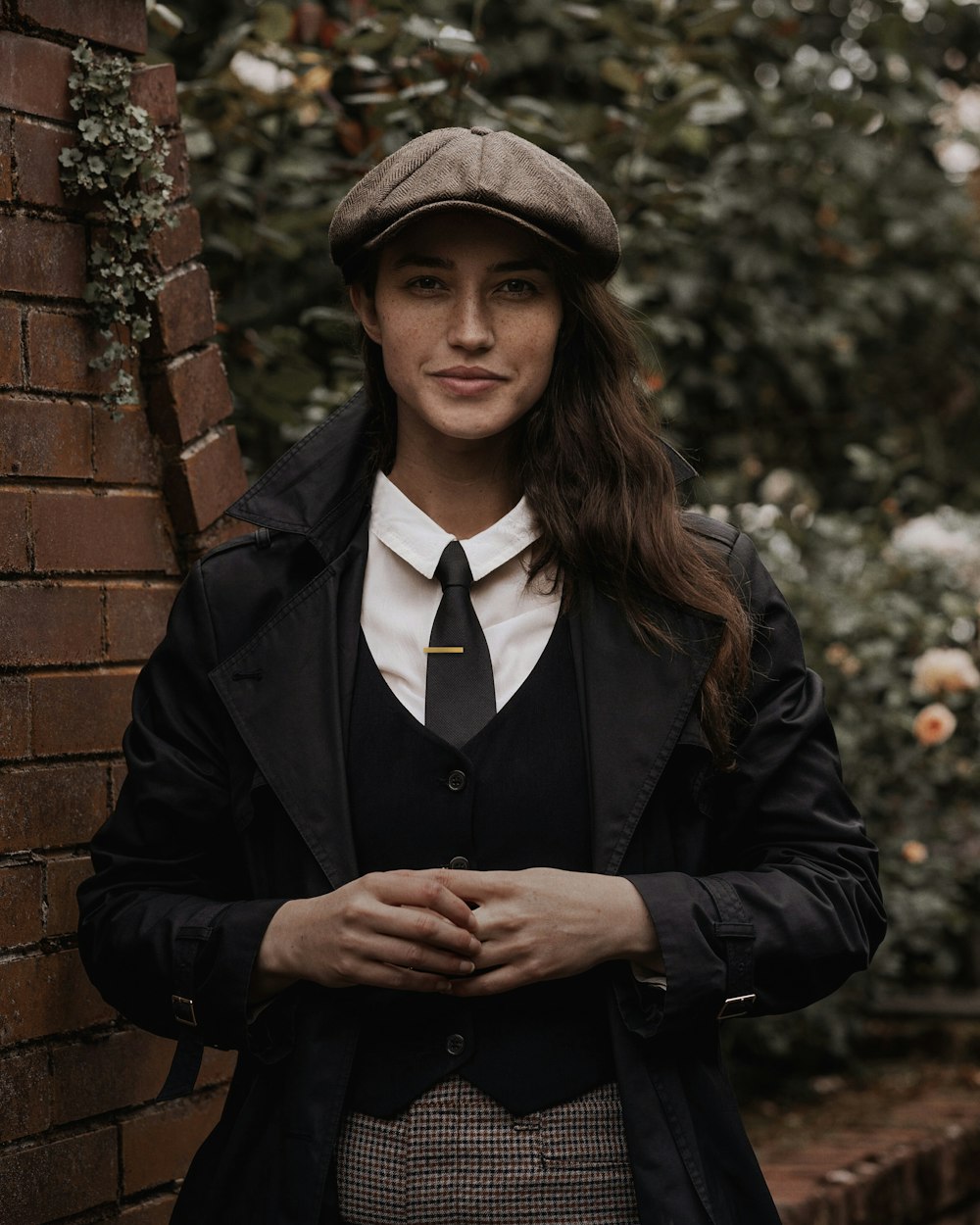 a woman wearing a suit and tie standing next to a brick wall