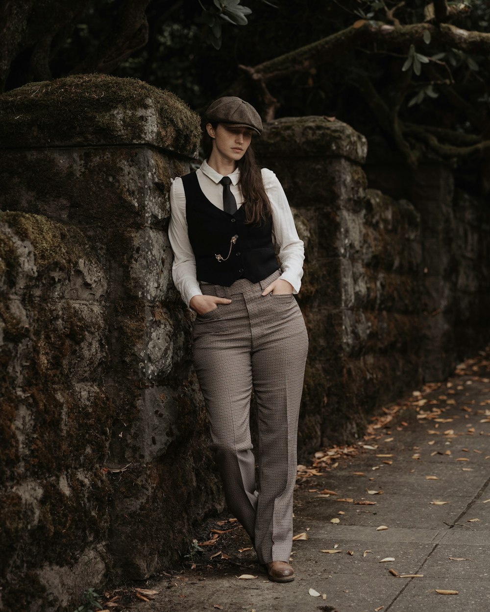 a woman leaning against a stone wall with her hands on her hips