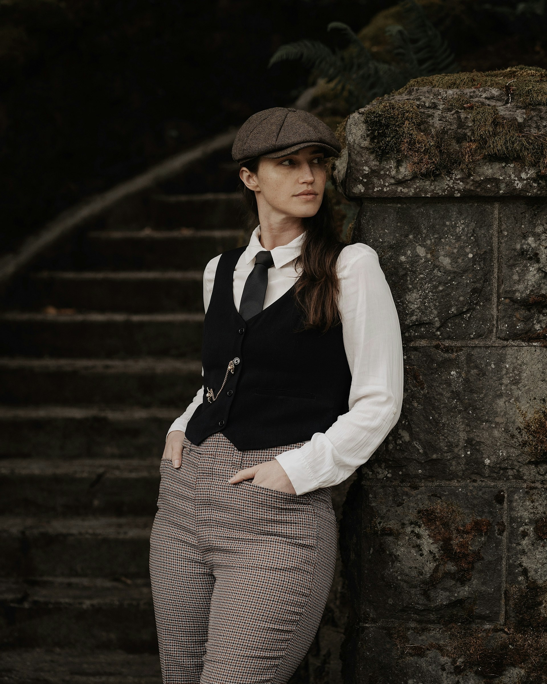 a woman leaning against a stone wall wearing a hat
