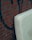 A light-colored mattress is leaning against a brick wall with graffiti. The wall is made of reddish-brown bricks with dark mortar lines. The graffiti features dark, abstract shapes.
