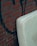 A light-colored mattress is leaning against a brick wall with graffiti. The wall is made of reddish-brown bricks with dark mortar lines. The graffiti features dark, abstract shapes.