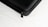 A close-up of a black textured hard case, featuring a zipper with a black pull tab. The background is a white surface with a subtle wood grain pattern.