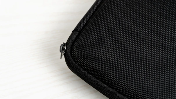 Close-up of a sleek black mini waist pack with silver zippers against a textured concrete wall.